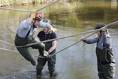 Outdoor Training: Mitarbeiter bei der Teamaufgabe "Bau einer Seilbrücke über einen Bach"