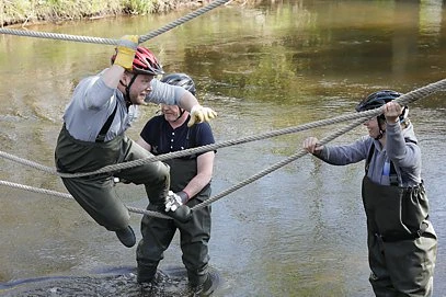 Outdoor Training: Mitarbeiter bei der Teamaufgabe "Bau einer Seilbrücke über einen Bach"