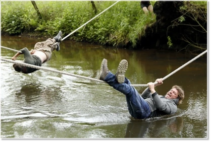 Outdoor-Abenteuer Seilbrückenbau: Mitarbeiter beim Versuch einen Bach zu überqueren