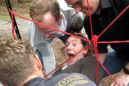 Mitarbeiterin beim Outdoor Teamtraining durchquert sogenanntes "Spinnennetz"